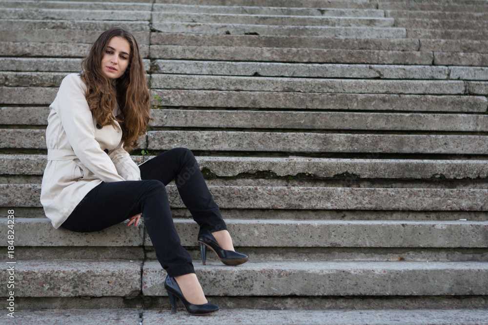 Young beautiful woman wearing beige jacket sitting on concrete stairs Young beautiful woman wearing beige jacket sitting on concrete stairs