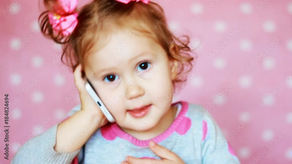 Beautiful cute little girl calls by mobile phone and talks. A funny child speaks on a smartphone, a close-up portrait Beautiful cute little girl calls by mobile phone and talks. A funny child speaks on a smartphone, a close-up portrait