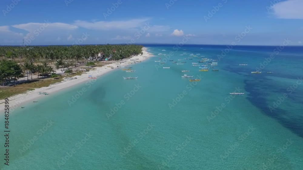 Lots of traditional Philippine fishing ships rest offshore next to a sandy beach, aerial shot Lots of traditional Philippine fishing ships rest offshore next to a sandy beach, aerial shot