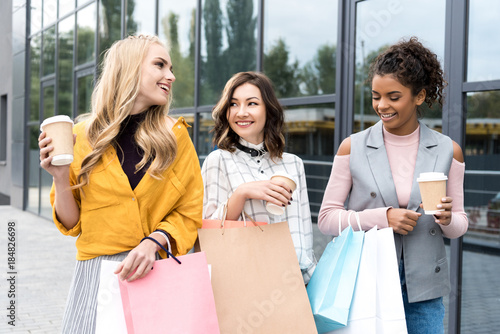 group of happy young women with shopping bags and coffee to go