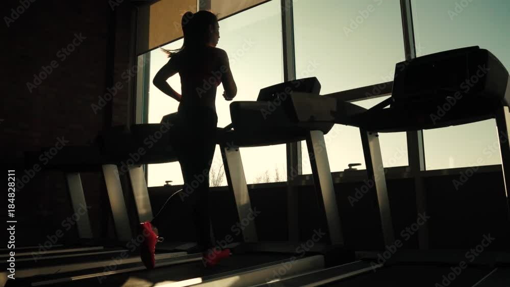silhouette of a girl on a treadmill. young sporty girl running on the treadmill at the gym. athlete in sportswear silhouette of a girl on a treadmill. young sporty girl running on the treadmill at the gym. athlete in sportswear