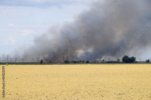 The fire is somewhere beyond the plowed field. Dark smoke from a fire. © eleonimages