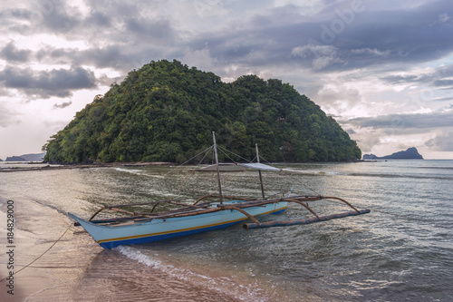 Bangka boat with Depeldel Island view from Las Cabanas beach at sunset in Palawan island, Philippines