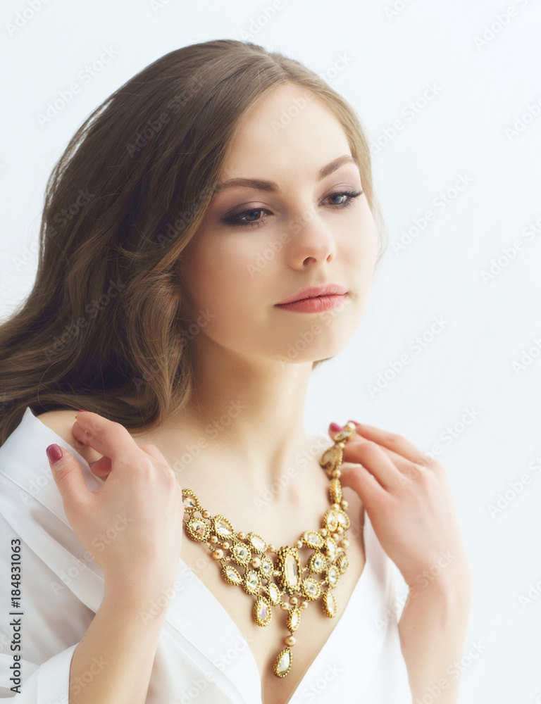 Beauty portrait of attractive and young woman trying golden necklace.