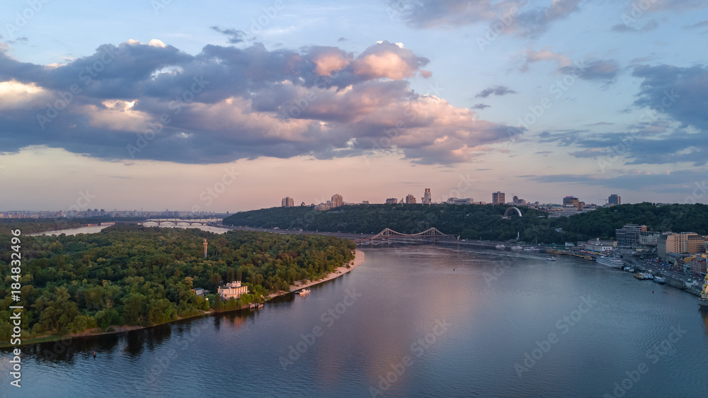 Aerial top view of Kiev city from above, Kyiv skyline, hills, pedestrian Park bridge and Dnieper river on sunset, Ukraine
