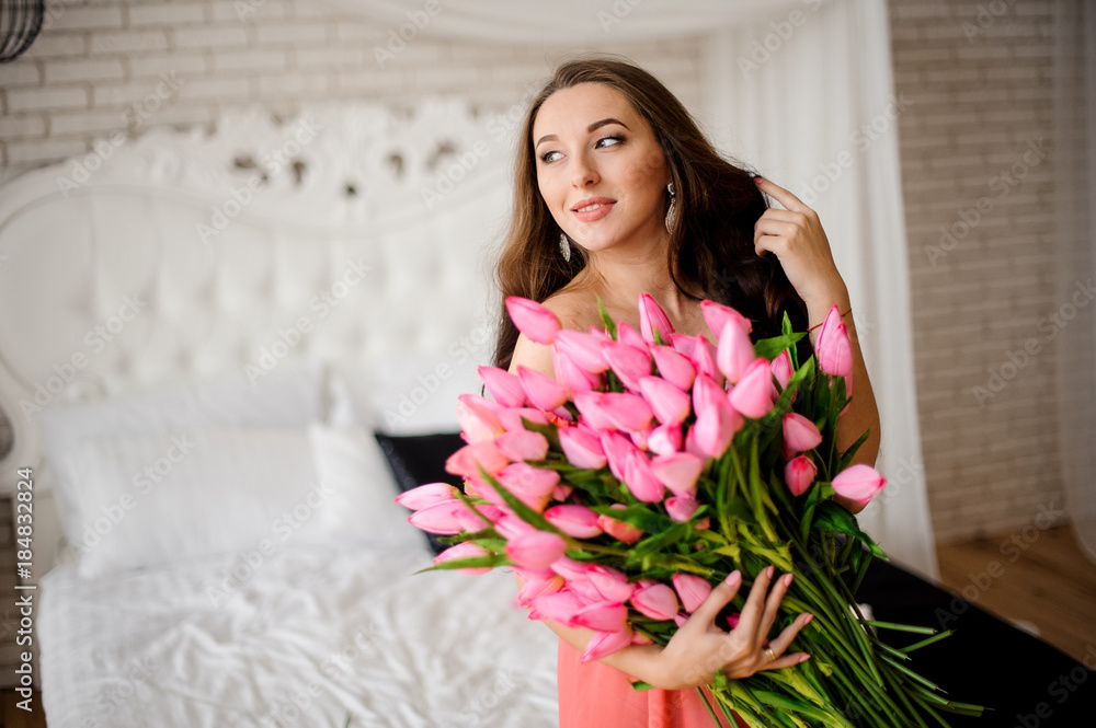 Beautiful long-haired woman sitting on the bed with bouquet of tulips Beautiful long-haired woman sitting on the bed with bouquet of tulips