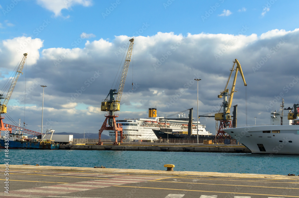 Fototapeta premium Heraklion, Crete, Greece - November, 2017: In the foreground - sea and pier of the port of Heraklion, loading equipment, cruise liner, cars, in the background - mountains