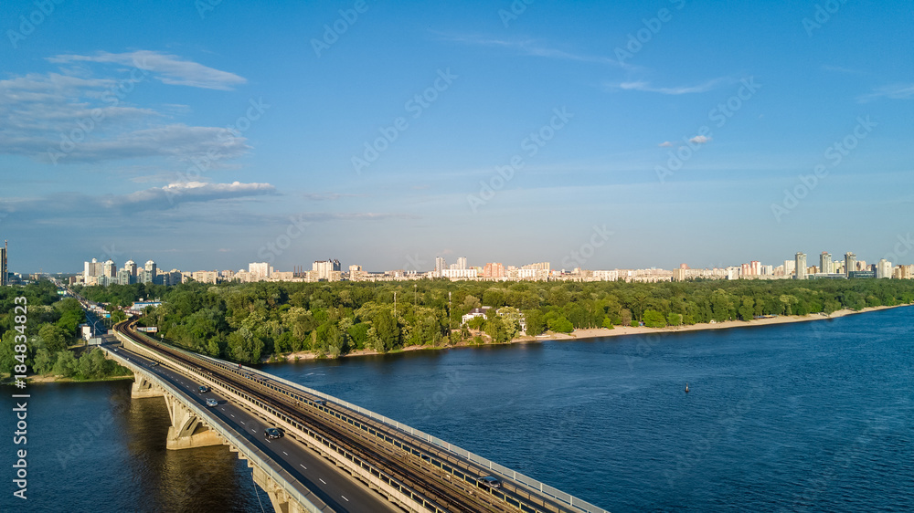 Aerial top view of Metro railway bridge with train and Dnieper river from above, skyline of city of Kiev, Ukraine
