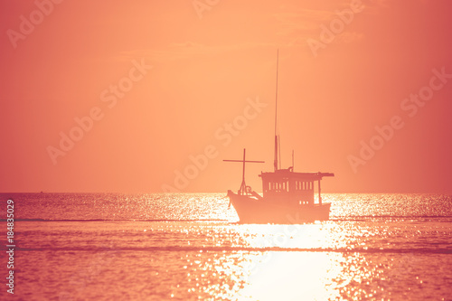 Beautiful seascape view of fishing boat floating on the sea with sunset light in the background. (Selective focus)