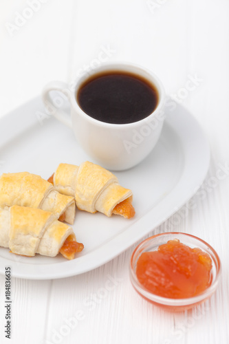 Freshly baked croissant, jam, cup of black coffee on white wooden background. Homemade cookie. Fresh pastries for breakfast. Delicious dessert. Closeup photography. Horizontal banner