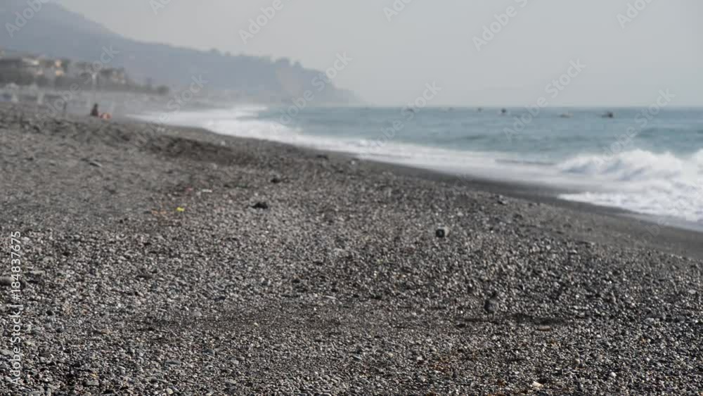 Piccioni sulla spiaggia con mare mosso mentre uomini osservano il mare