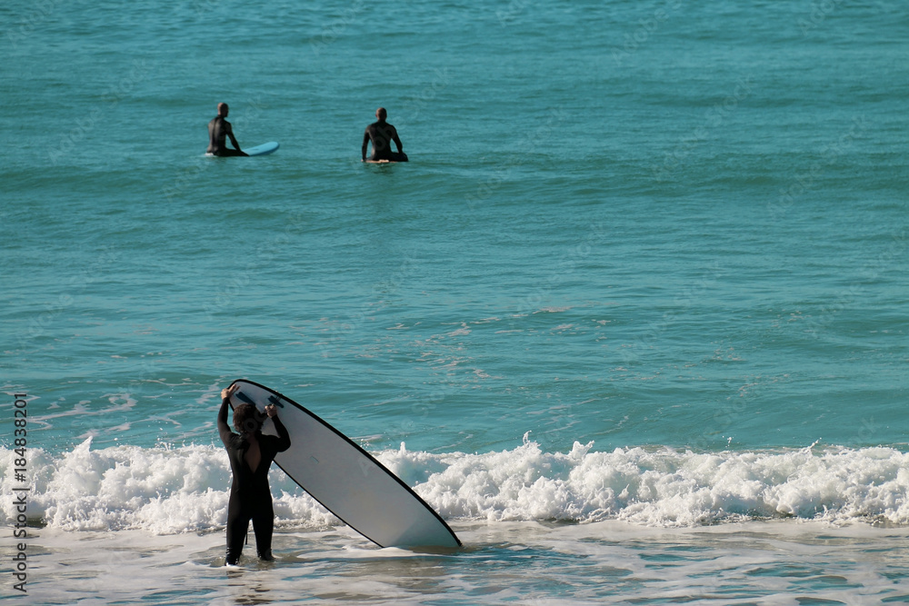Naklejka premium A man carrying his board to surf with other surfers on the beach of El Palmar, on the coasts of Cadiz, Spain