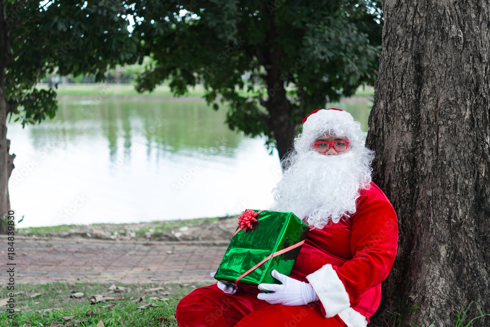 Obraz premium Santa claus with gift box sit under tree,Thailand people,Sent happiness for children,Merry christmas,Welcome to winter