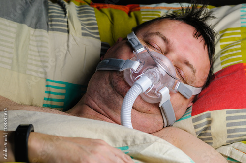 A middle-aged, overweight man wearing a CPAP mask while sleeping in bed photo