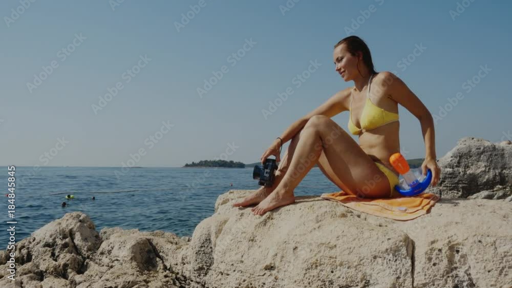 Woman with snorkelling mask and camera sitting on rock Woman with snorkelling mask and camera sitting on rock