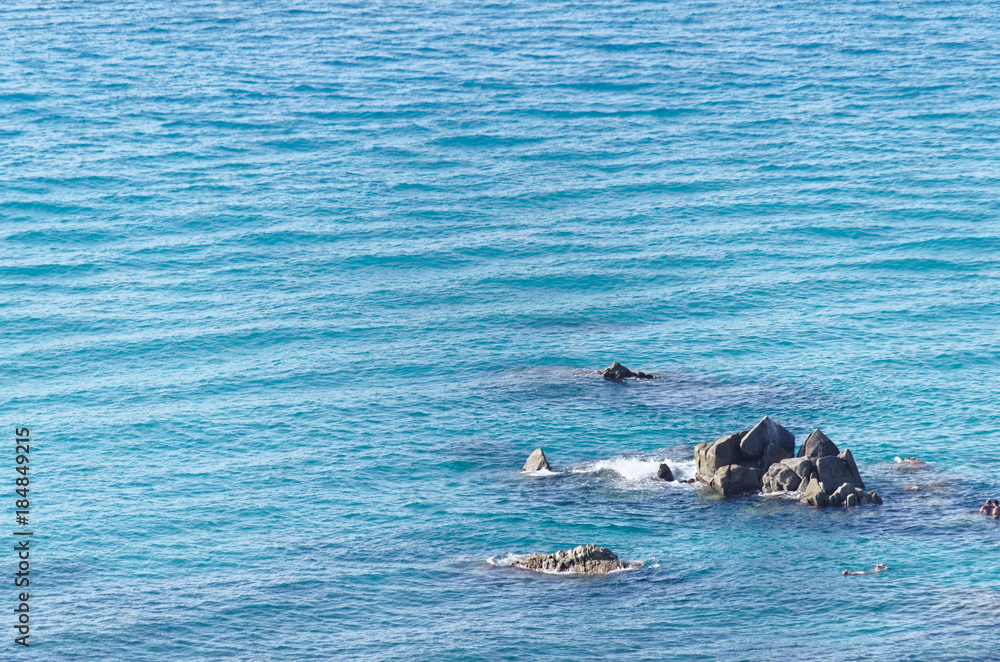Fototapeta premium Pointed rocks in the blue water of tyrrhenian sea, near beach in tropea