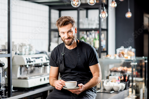 Portrait of a handsome barista sitting with coffee at the bar of the modern cafe interior photo