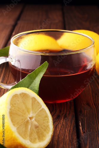 Glass cup of hot tea with lemon on brown wooden background