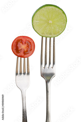 Lime and tomato on silver forks, white background