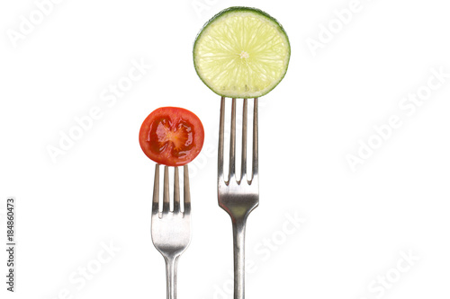 Lime and tomato on silver forks, white background