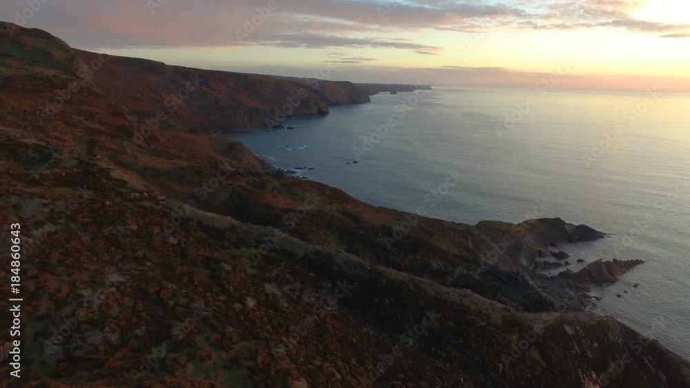 The sun sets along the coast of Devon and Cornwall in South West England. Aerial from drone. The sun sets along the coast of Devon and Cornwall in South West England. Aerial from drone.