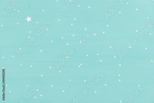 turquoise wooden background with small shiny silver stars. Holidays, Christmas or any other celebration.