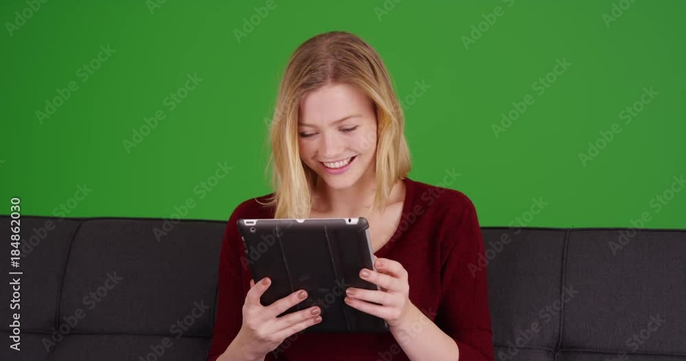 Attractive beautiful Caucasian woman laughing on a couch and looking at a digital pad on green screen. On green screen to be keyed or composited. Attractive beautiful Caucasian woman laughing on a couch and looking at a digital pad on green screen. On green screen to be keyed or composited.