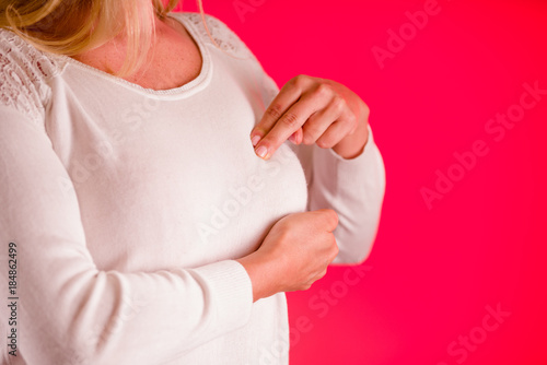Closeup cropped portrait young woman with breast pain touching chest, on pink background