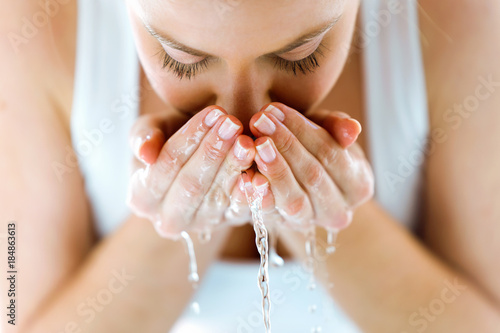 Beautiful young woman washing her face splashing water in a home bathroom.