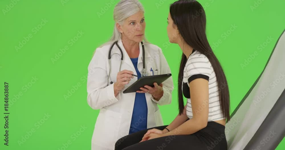 An older doctor gives a check up while using her tablet on green screen. On green screen to be keyed or composited. An older doctor gives a check up while using her tablet on green screen. On green screen to be keyed or composited.