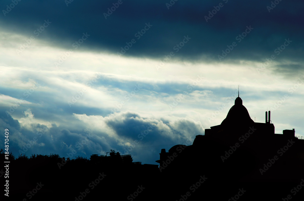 silhouette of the building with the spire in the background of storm clouds