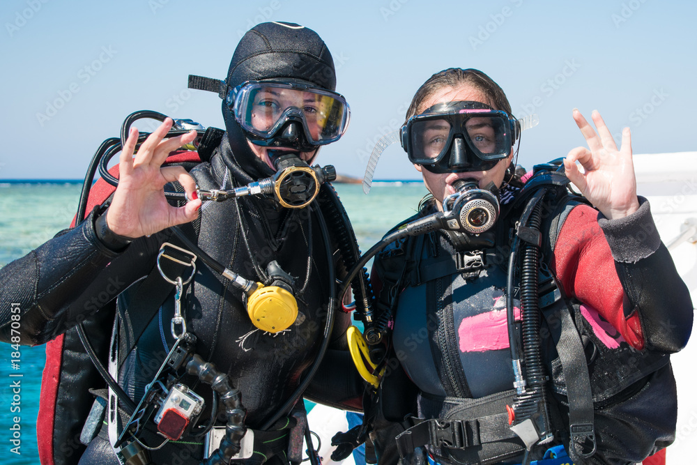 two happy divers in wetsuits and masks with octopus in mouthes on the background of azure sea show ok . happy girls in wetsuits. scuba diving. diving. divers