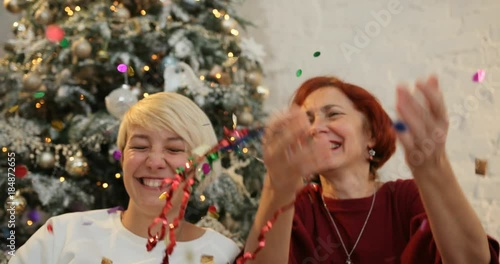 Mother and daughter being excited with sparkling colorful confetti falling all around, christmas tree background. Christmas holiday and New Year. photo