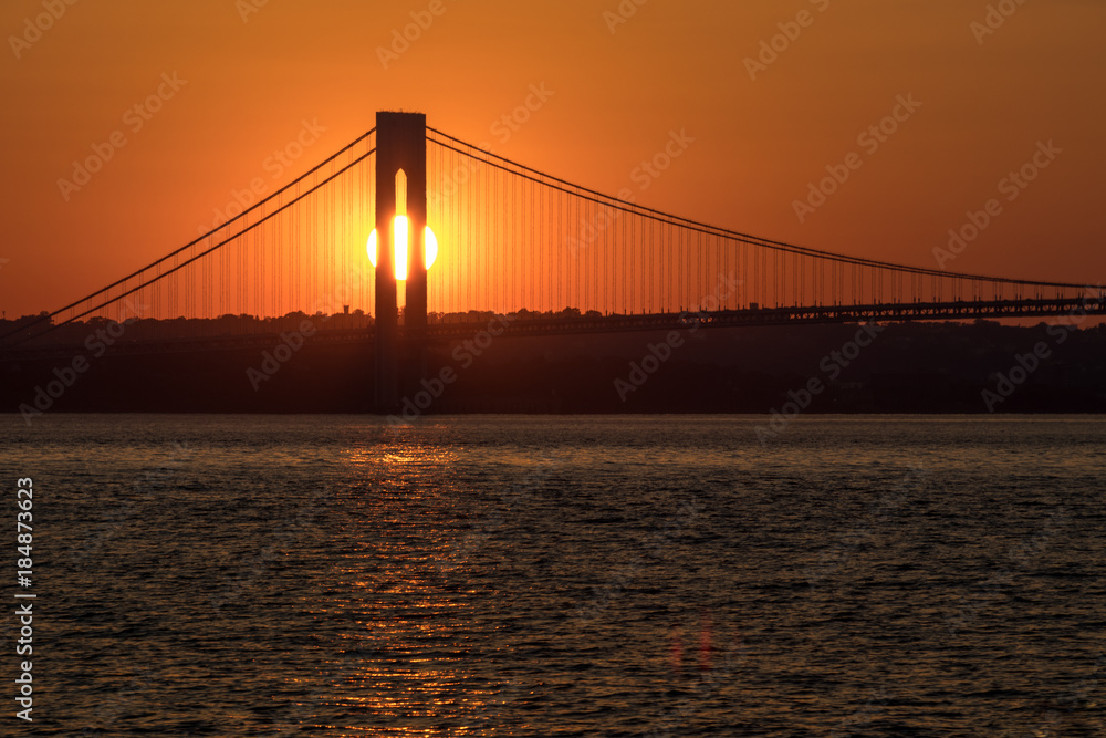 Sunset over horizon behind big bridge, red sunlight background, sun path on water