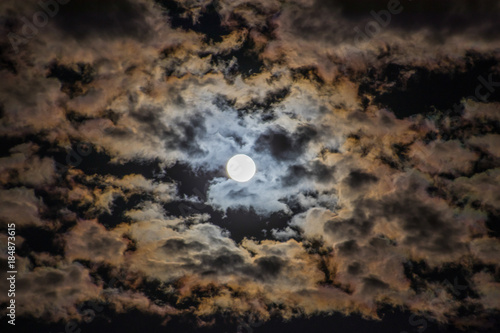 Bright moon in the night sky surrounded by colorful clouds
