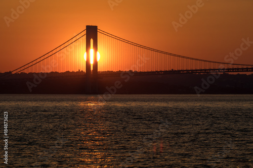 Sunset over horizon behind big bridge, red sunlight background, sun path on water