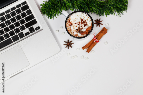 Flat lay home office desk workspace with laptop, a cup of hot chocolate topping with marshmallow and gift box on white background. Top view. Christmas background.