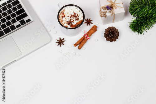 Flat lay home office desk workspace with laptop, a cup of hot chocolate topping with marshmallow and gift box on white background. Top view. Christmas background.