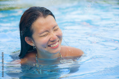 happy and pretty Chinese Asian woman enjoying cheerful and relaxed having fun smiling at swimming pool of resort hotel in Summer holiday