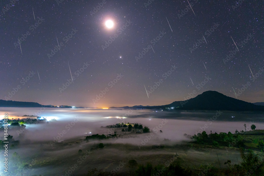 Fototapeta premium Geminid Meteor in the night sky with moon and fog at Khao Takhian Ngo View Point at Khao-kho Phetchabun,Thailand