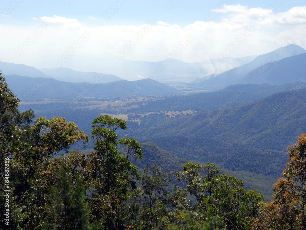A birds eye view of a valley from the Atherton Tablelands towards Innisfail in Queensland, Australia showing a bush fire in the distance    