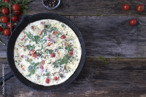 A beautiful omelette with greens, tomatoes and spices in an old frying pan. Space for copy space.