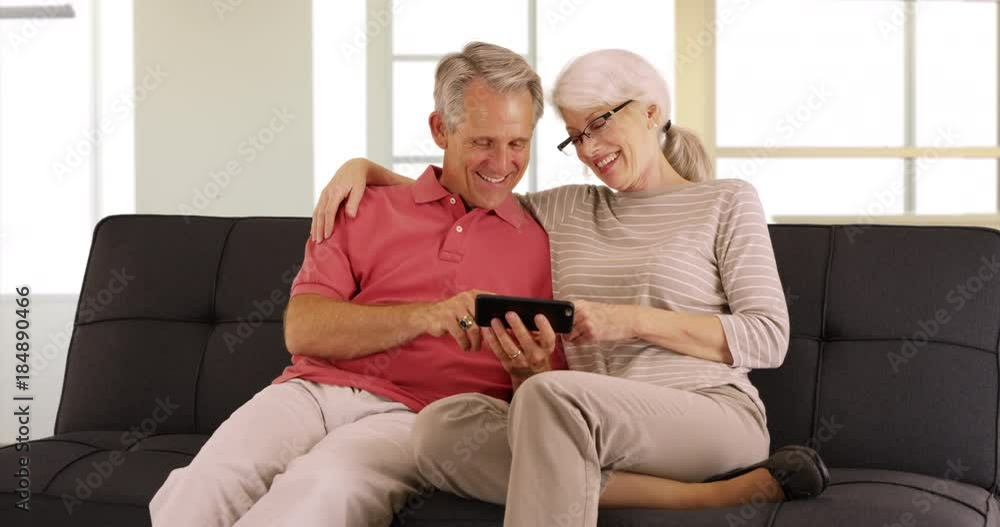 Happy seniors sitting on couch watching videos on smartphone Happy seniors sitting on couch watching videos on smartphone