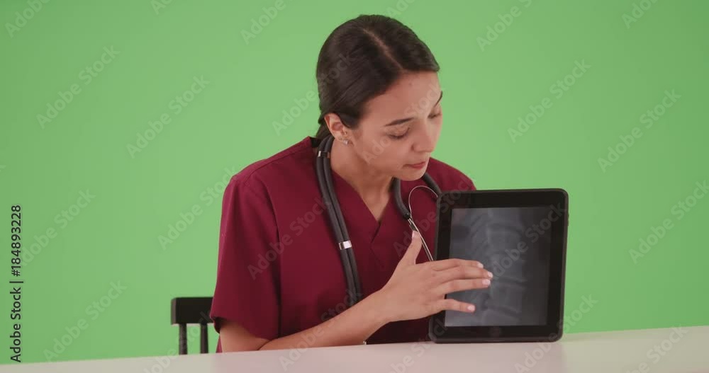 Hispanic female nurse or doctor on greenscreen sitting at table explaining x-ray on tablet computer. Medical professional using technology to share xray of spine for chroma key or compositing. 4k Hispanic female nurse or doctor on greenscreen sitting at table explaining x-ray on tablet computer. Medical professional using technology to share xray of spine for chroma key or compositing. 4k