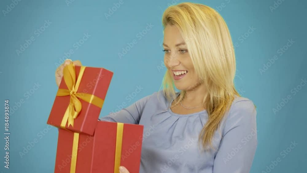Wondered cute blonde young woman opening red gift box over blue background Wondered cute blonde young woman opening red gift box over blue background