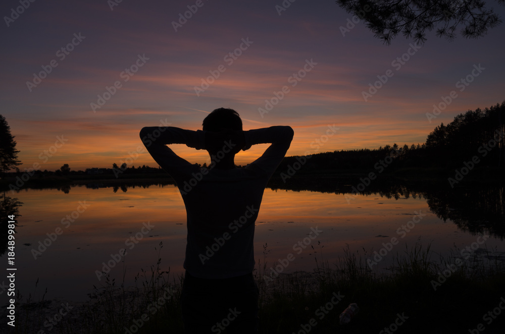 Fototapeta premium Man looking at sunset at the lake holding hands behind his head