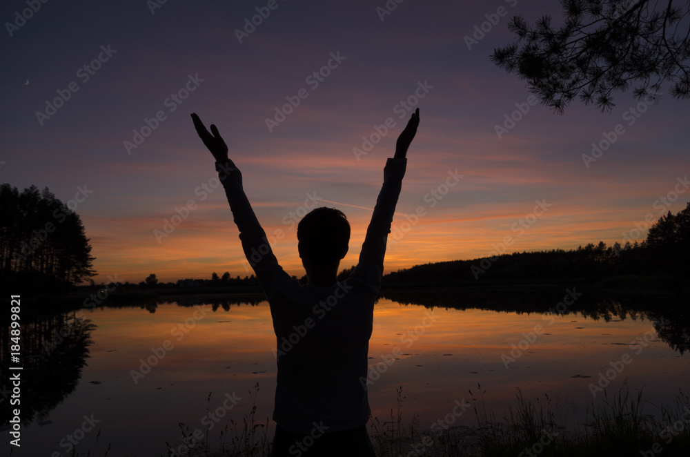 Man greeting sunset standing near the lake and