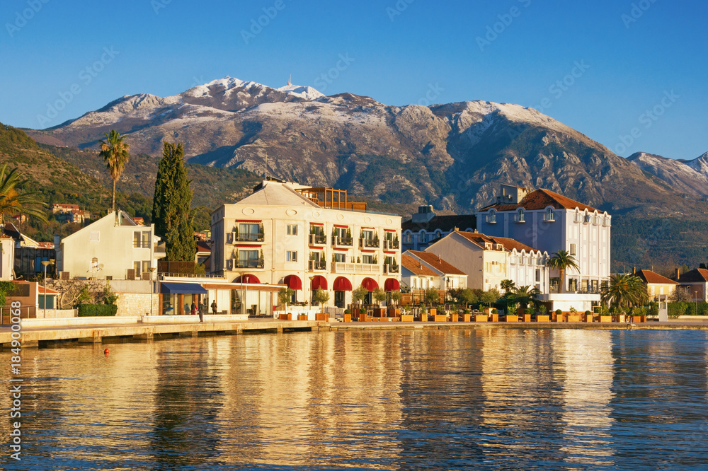 Sunny winter day in Montenegro. Embankment of Tivat city and snow-capped peaks of Lovcen mountain