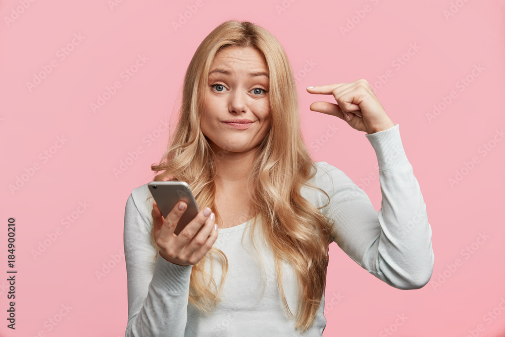Photo of blue eyed female with light hair, recieve message on smart phone, shows size of her salary, being confused, isolated over pink background. Attractive woman poses with modern electronic gadget Photo of blue eyed female with light hair, recieve message on smart phone, shows size of her salary, being confused, isolated over pink background. Attractive woman poses with modern electronic gadget