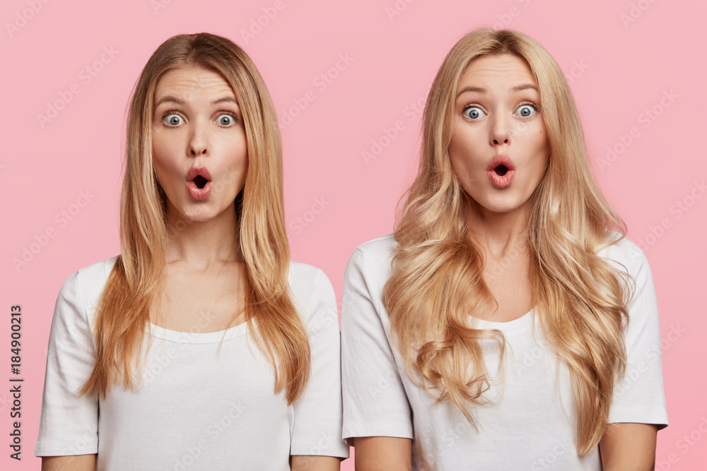 Two surprised blonde sisters stand next to each other, keep mouth opened and stare at camera, dressed casually, shocked to recieve bad shocking news from parents. Amazed females isolated on pink wall Two surprised blonde sisters stand next to each other, keep mouth opened and stare at camera, dressed casually, shocked to recieve bad shocking news from parents. Amazed females isolated on pink wall